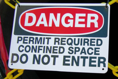 Danger sign warning against entry without a confined space permit in front of a dark opening