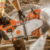 Close-up of a worker using a demolition saw on construction material, with water suppression system reducing dust