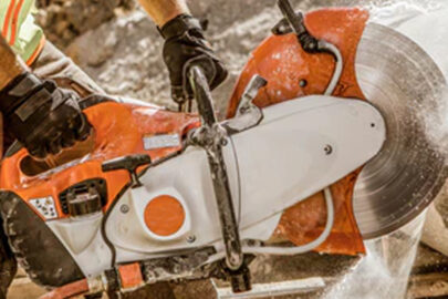 Close-up of a worker using a demolition saw on construction material, with water suppression system reducing dust