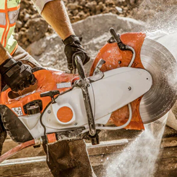 Close-up of a worker using a demolition saw on construction material, with water suppression system reducing dust